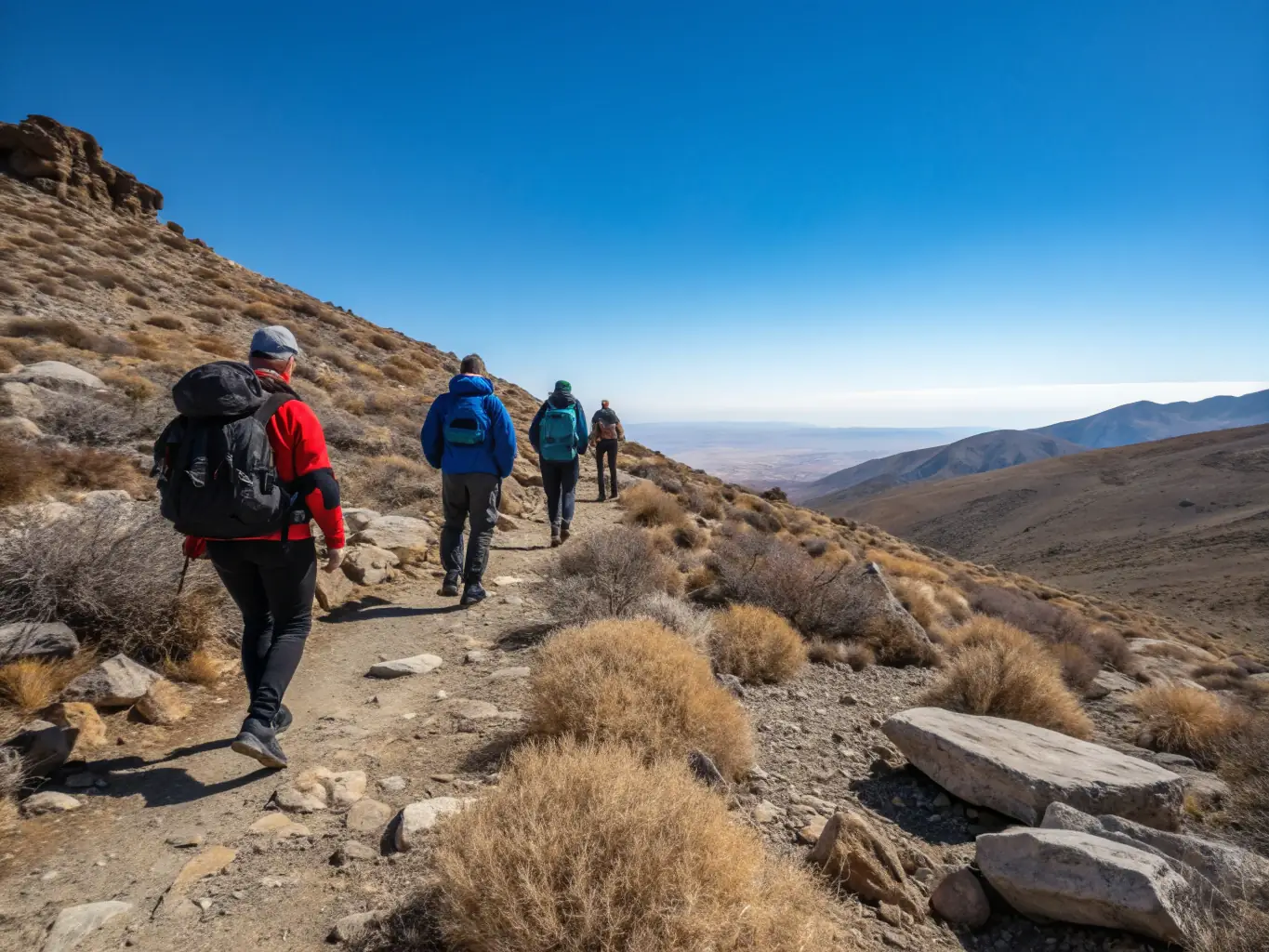 A photograph captures a group of experienced hikers navigating a challenging mountain trail in the Sumene region. The terrain is rocky, and the hikers are using trekking poles for stability. The sky is clear, and the view from the summit is breathtaking.